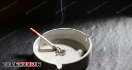 دانلود عکس استوک : سیگار در حال سوختن در جا سیگاری Lit Cigarette Lying On An Empty White Ashtray
