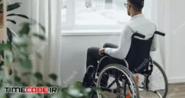 دانلود عکس مرد روی ویلچر کنار پنجره Young Disabled Man Sitting In A Wheelchair Near The Window At Home