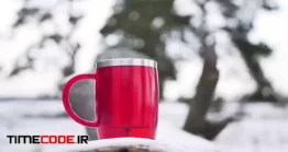 دانلود فوتیج چای داغ در ماگ قرمز Red Mug Of Tea On A Wooden Branch In The Winter Morning