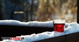 دانلود فوتیج لیوان چای داغ در زمستان Steaming Tea In A Glass Standing On Snow At Tree Branch