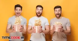 دانلود عکس مردان جوان در حال تماشای فیلم و خوردن پاپ کورن Three Young Happy Men Eating Popcorn